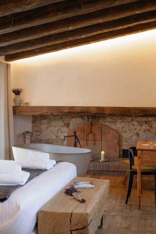 Lujoso cuarto de baño en Mas Escarrà con bañera exenta, chimenea de piedra vista y vigas de madera oscura en Caldes de Malavella