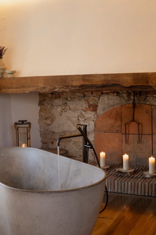 Baño lujoso del hotel Mas Escarrà con chimenea de piedra, bañera exenta y ambiente iluminado por velas en Caldes de