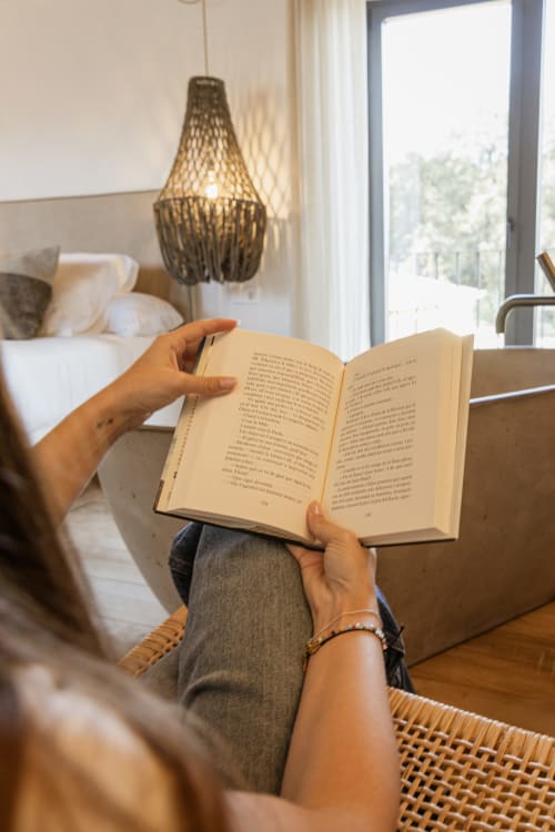 Huésped leyendo un libro en la habitación L'Estudi del hotel Mas Escarrà en Caldes de Malavella, con lámpara colgante moderna y vista al dormitorio