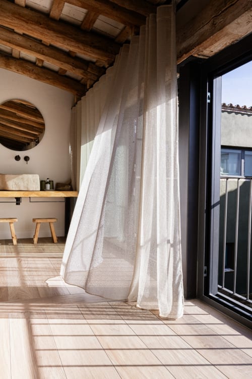 Habitación L'Assecador en Mas Escarrà con vigas de madera, cortinas semitransparentes, espejo circular y acceso a terraza
