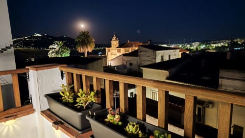 Terraza Medieval Mirador de noche con plantas suculentas, barandillas de madera, vistas a los tejados históricos de Cáceres iluminados por la luna