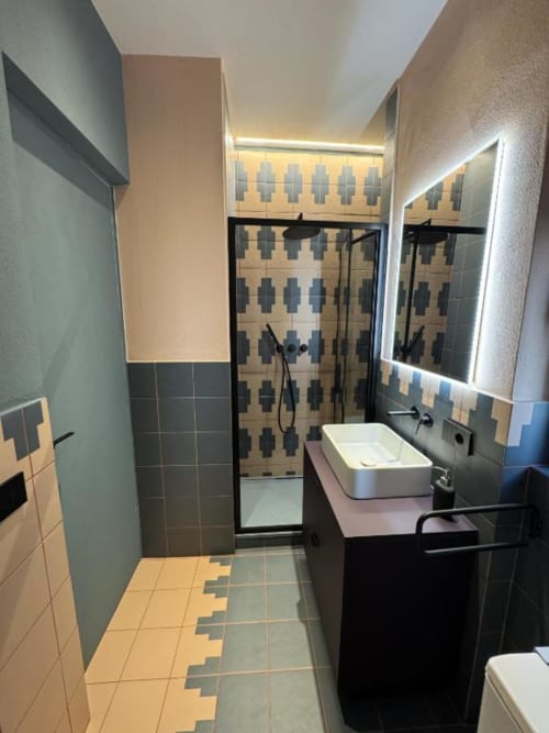 Bagno moderno nell'appartamento milanese con piastrelle geometriche, lavabo da appoggio, specchio illuminato e doccia walk-in presso Muratori