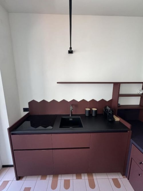 Moderna cucina nel monolocale di Milano a Muratori con mobili bordeaux e piano di lavoro nero