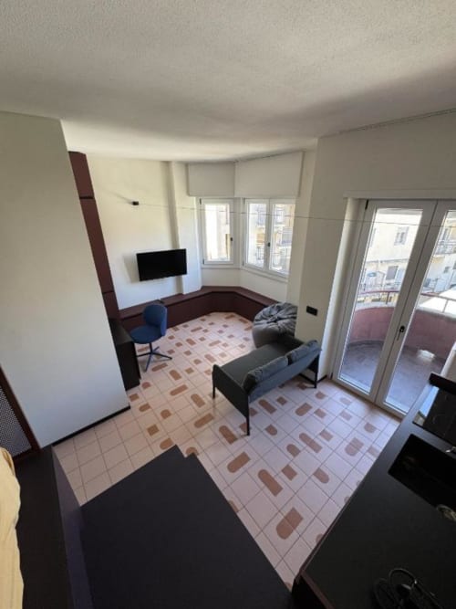 Monolocale ad Aparthotel Muratori Milano con letto, TV, poltrona blu e balcone con vista sulla città