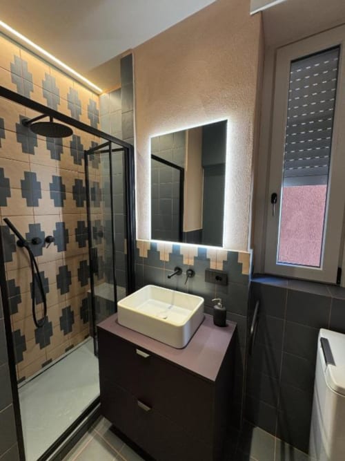 Bagno moderno presso Muratori Apartments Milano con doccia in piastrelle geometriche, specchio illuminato e vanity rosa