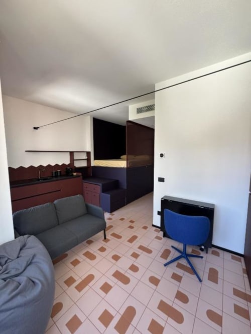 Monolocale moderno presso Muratori Apartments Milano con divano grigio, angolo cottura e letto sullo sfondo