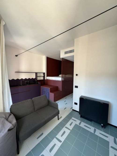 Monolocale moderno presso Muratori Apartments Milano con divano, TV, angolo cottura e letto rialzato