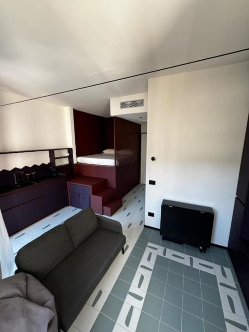 Monolocale presso Muratori Apartments Milano con divano, letto in legno scuro e pavimentazione in piastrelle moderne