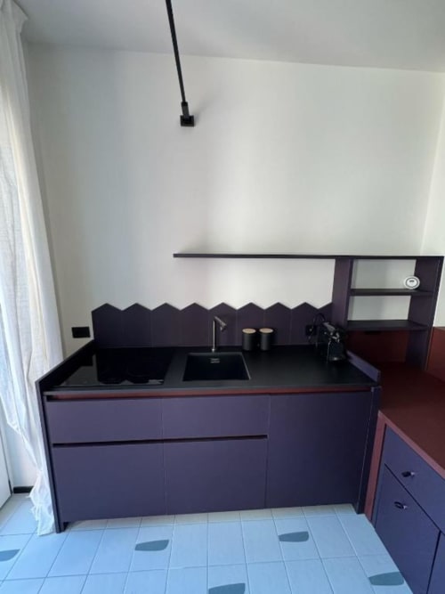 Moderna cucina con piano lavoro nero e mobili scuri nello studio Muratori Apartments a Milano
