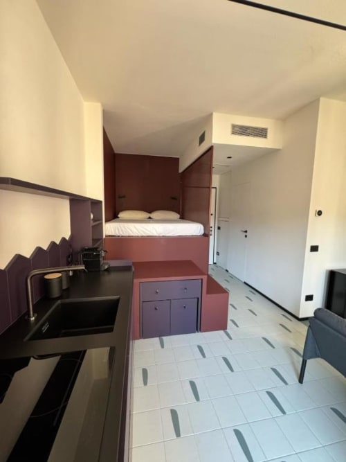 Monolocale moderno a Muratori Apartments Milano con letto rialzato, angolo cottura e pavimento in ceramica