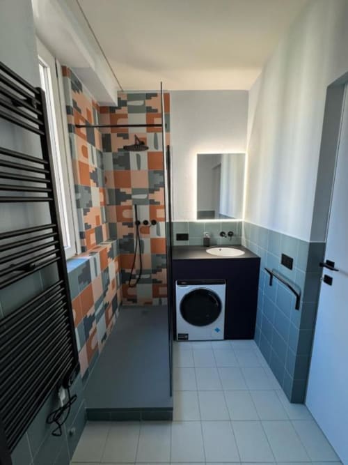 Moderno bagno degli Aparthotel Muratori Milano con doccia con piastrelle colorate, scaldasalviette nero e lavatrice integrata