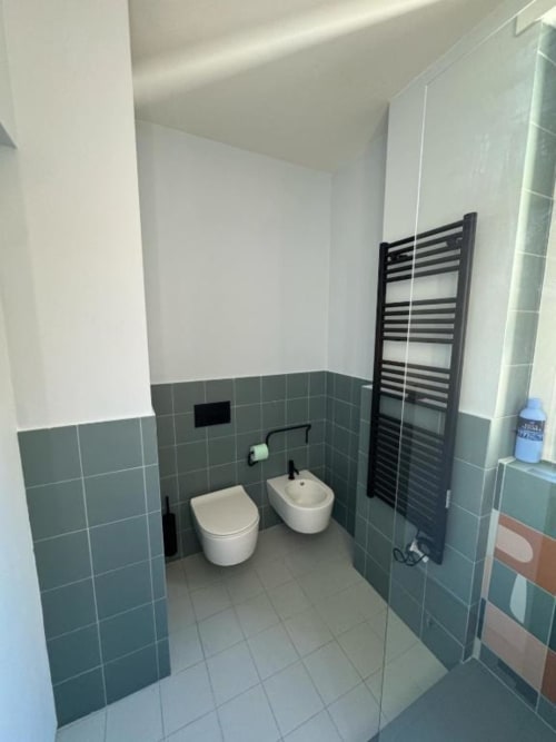 Bagno moderno presso Muratori Apartments Milano con toilette, bidet, portasciugamani nero e pareti con piastrelle verdi