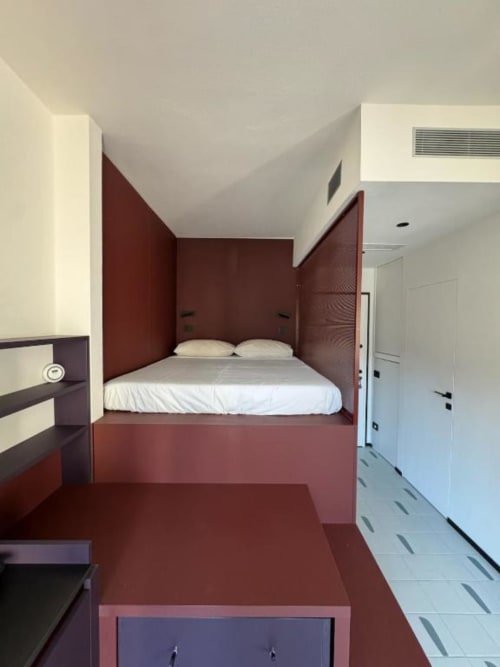 Camera da letto moderna a Muratori Apartments Milano con letto rosso integrato e biancheria bianca