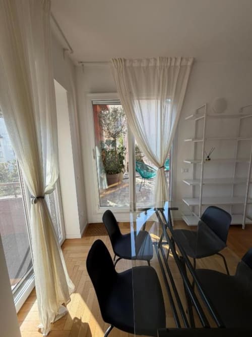 Corridoio moderno con sedie nere, tende color crema e vista sulla terrazza degli Apartamenti Muratori Milano