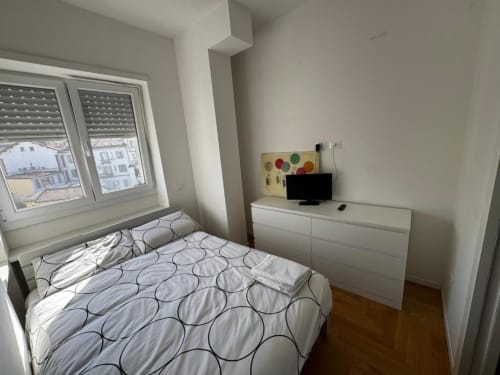 Camera moderna a Muratori Apartments Milano con letto matrimoniale, cassettone bianco, TV e finestre con vista sulla città