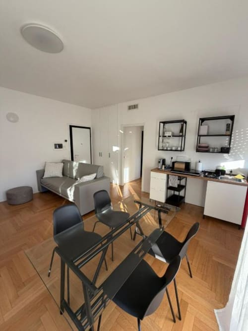Interno moderno dell'appartamento a Milano con tavolo da pranzo, angolo cucina, divano grigio e sedie nere presso Muratori Apartments