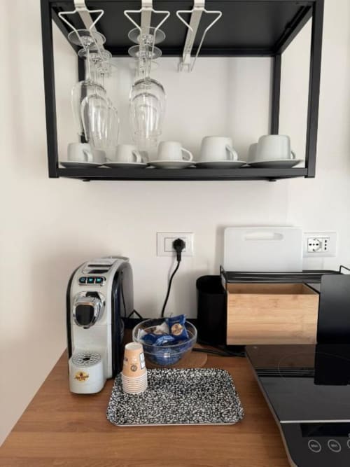 Angolo cottura moderno nell'appartamento milanese con macchina per espresso, scaffale in vetro a parete, tazze bianche e elettrodomestici compatti