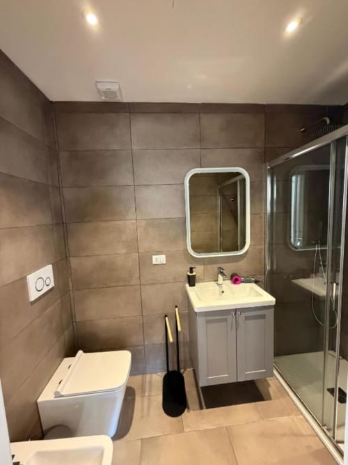 Bagno moderno presso Muratori Apartments Milano con vanità contemporanea, specchio LED, doccia e piastrelle beige