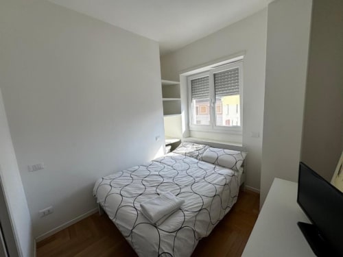 Camera moderna negli Appartamenti Muratori Milano con letto matrimoniale, scaffali, finestra con persiane e pavimento in legno