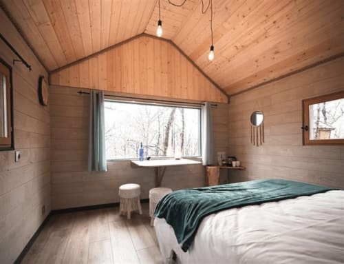 Cozy wooden bedroom at Les Murmures du Bois with queen bed, pendant lights, and garden views through large windows