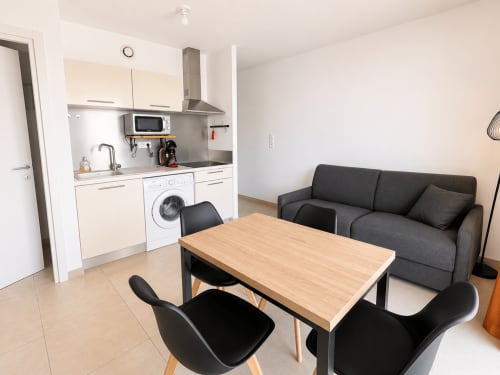 Séjour d'un studio moderne avec kitchenette, table à manger, chaises noires et canapé anthracite à Résidence Marina di