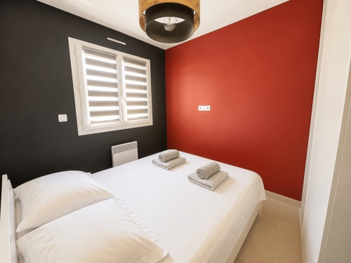 Chambre moderne à Marina di Bravone avec mur d'accent rouge, mur noir, lit blanc, serviettes roulées et fenêtre à volets