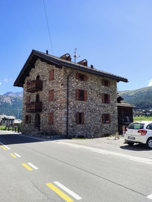 Stone hotel building Al Dos in Livigno with wooden balconies, mountain views, and parked car on sunny day