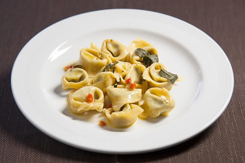Eleganti tortellini con salvia e peperone rosso su piatto bianco all'Hotel Ristorante alle Querce di Castelbuono