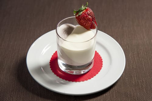 Elegante dessert con cremosa panna cotta, fragola fresca e sottobicchiere rosso all'Hotel Ristorante alle Querce di Castelbuono