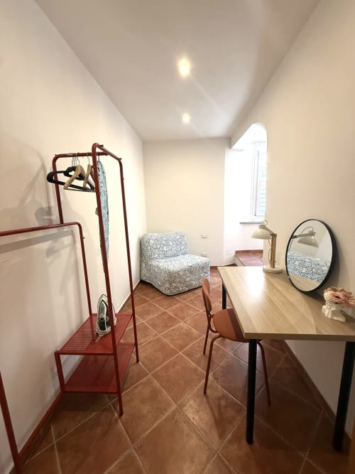 Camera moderna negli Appartamenti Castelli con scrivania, sedia, poltrona a motivi e appendiabiti rosso ad Albano Laziale