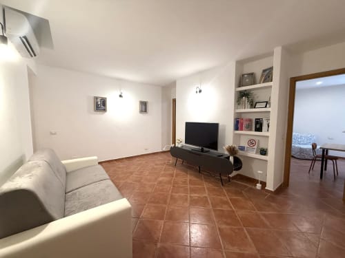Soggiorno moderno dell'appartamento familiare presso Castelli Apartments ad Albano Laziale con pareti bianche, pavimenti in cotto e TV