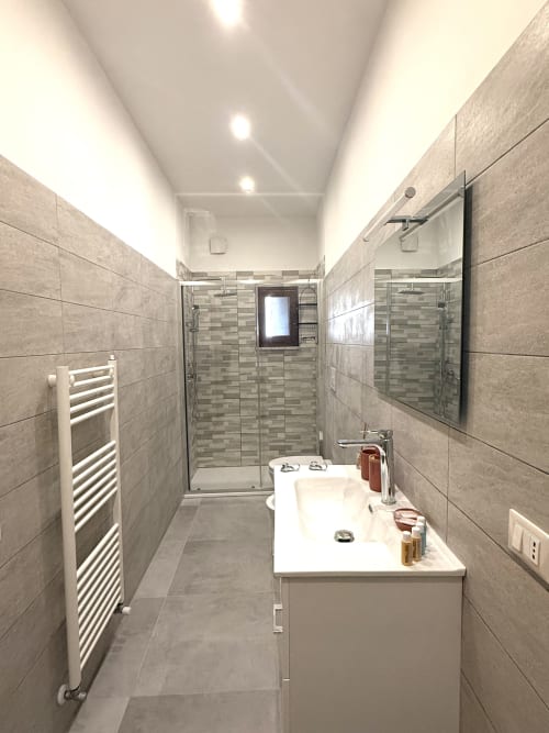 Bagno moderno negli Castelli Apartments con piastrelle grigie, doccia passante, vanità bianca e scaldasalviette