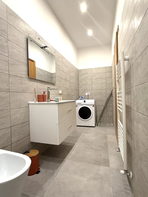 Bagno moderno presso Castelli Apartments con lavabo bianco, lavatrice, scaldasalviette e piastrelle grigie