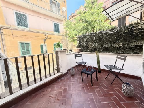 Terrazza esterna degli Appartamenti Castelli ad Albano Laziale con sedute, muri ricoperti d'edera e edifici storici.