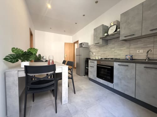 Cucina-soggiorno moderna a Castelli Apartments ad Albano Laziale con mobili grigi, tavolo da pranzo e acciaio inossidabile