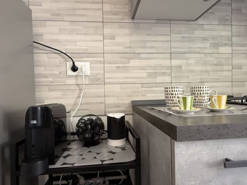 Moderna cucina in Castelli Apartments con piastrelle effetto legno, macchina caffè, tazze e elettrodomestici neri su bancone grigio