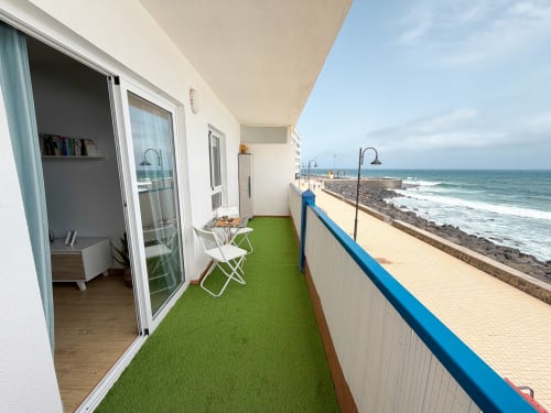 Balcony with green artificial turf, white chairs, and beachfront sea view at Haller Homes, Bajamar
