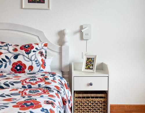 Acogedora habitación en Haller Homes Bajamar con ropa de cama floral, mesita de noche blanca y marco decorativo