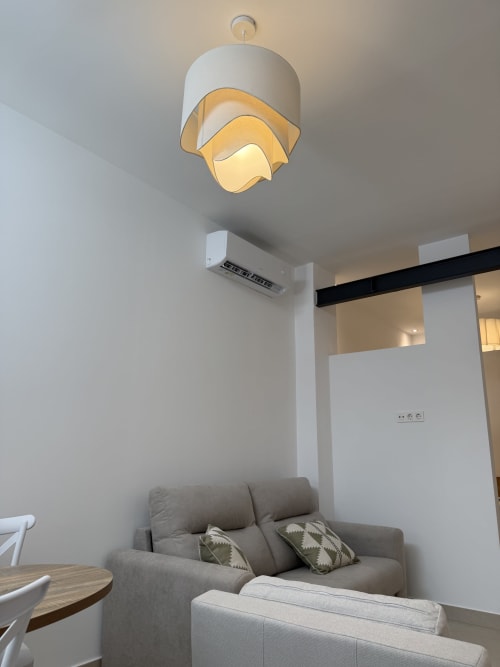 Modern hotel room in Cádiz with pendant light, gray sofa, and air conditioning unit