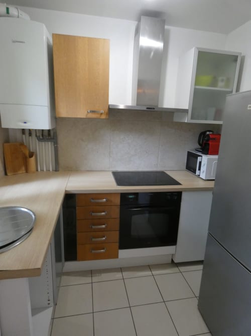 Cuisine moderne de l'appartement Sci Ludji avec armoires en bois et blanc, plaque de cuisson noire, appareils en acier inoxydable et carrelage