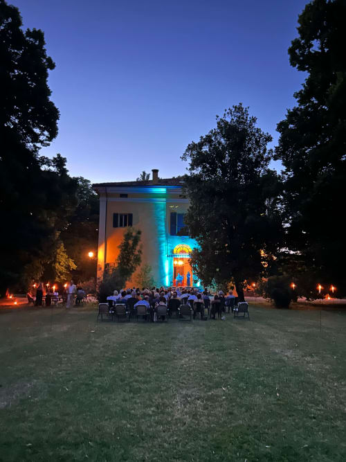 Evento serale all'aperto a Palazzo Bonfiglioli, San Giovanni in Persiceto, con edificio illuminato e ospiti seduti sul prato