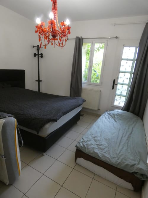 Chambre lumineuse de l'appartement Sci Ludji avec deux lits, lustre rouge, portes sur jardin et design accessible à Nanterre