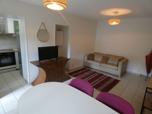 Appartement Sci Ludji à Nanterre : salon avec canapé, TV, table à manger blanche, commode bois et vue sur jardin