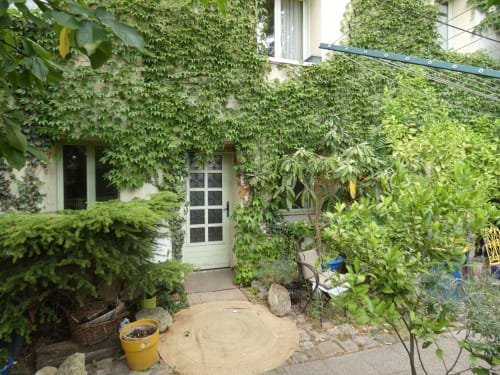 Entrée luxuriante de l'Appartement Jardin à Sci Ludji à Nanterre, porte crème, mobilier de jardin et jardinière jaune