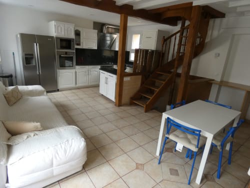Cuisine ouverte et séjour avec électroménagers inox, placards blancs, escalier en bois et coin repas