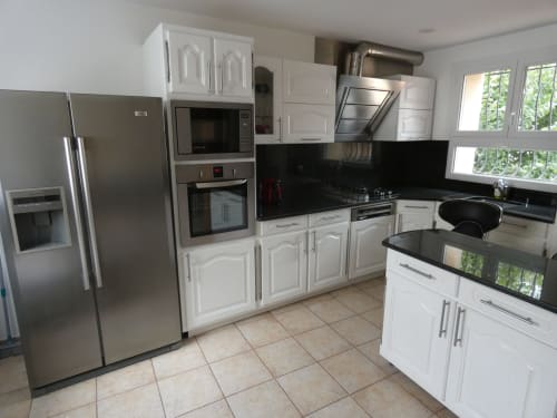 Cuisine moderne avec meubles blancs, électroménagers inox, plans de travail noirs et carrelage à la villa Sci Ludji