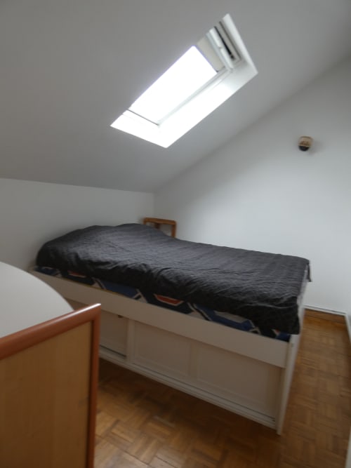 Chambre lumineuse sous les toits à la villa Sci Ludji à Nanterre avec puits de lumière, lit simple, mobilier en bois et vue sur le jardin
