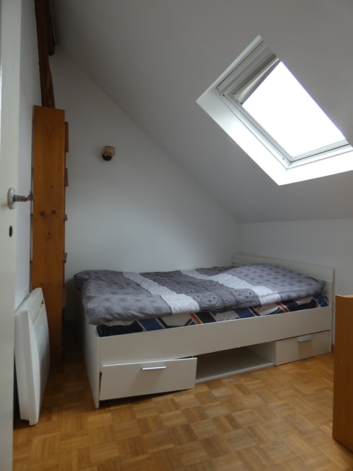 Chambre mansardée lumineuse à la villa Sci Ludji à Nanterre avec puit de lumière, lit blanc, porte bois et parquet