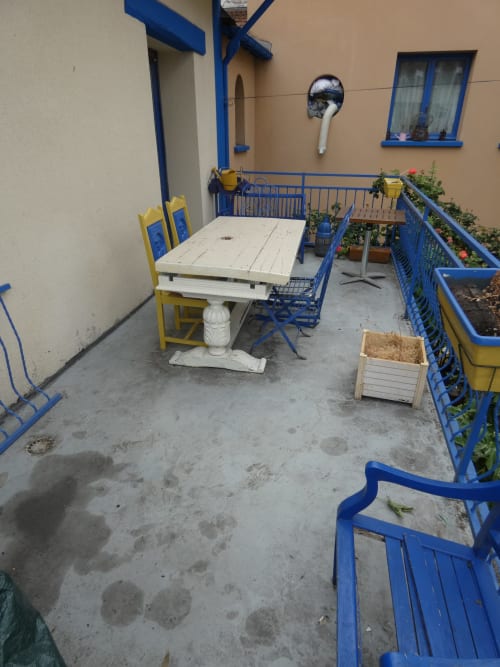 Terrasse de la villa Sci Ludji à Nanterre avec balustrades bleues, table blanche, chaises jaunes et plantes en pots