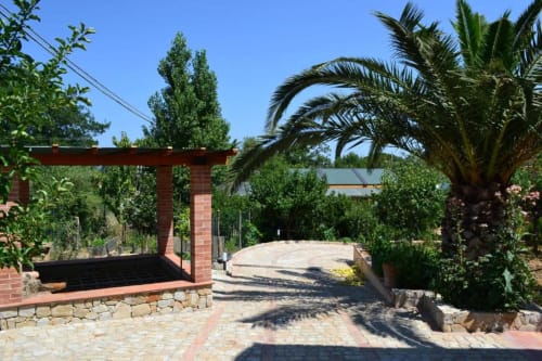 Cortile dell'Hotel Ristorante alle Querce a Castelbuono con pergolato in laterizio, palma e pavimentazione sotto cielo azzurro